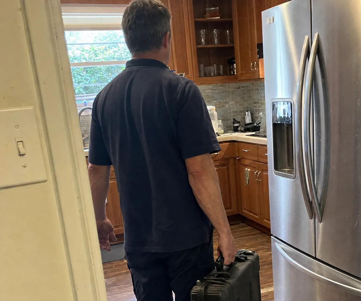 Left-hand crop of a kitchen doorway with a technician stepping through toward the appliances
